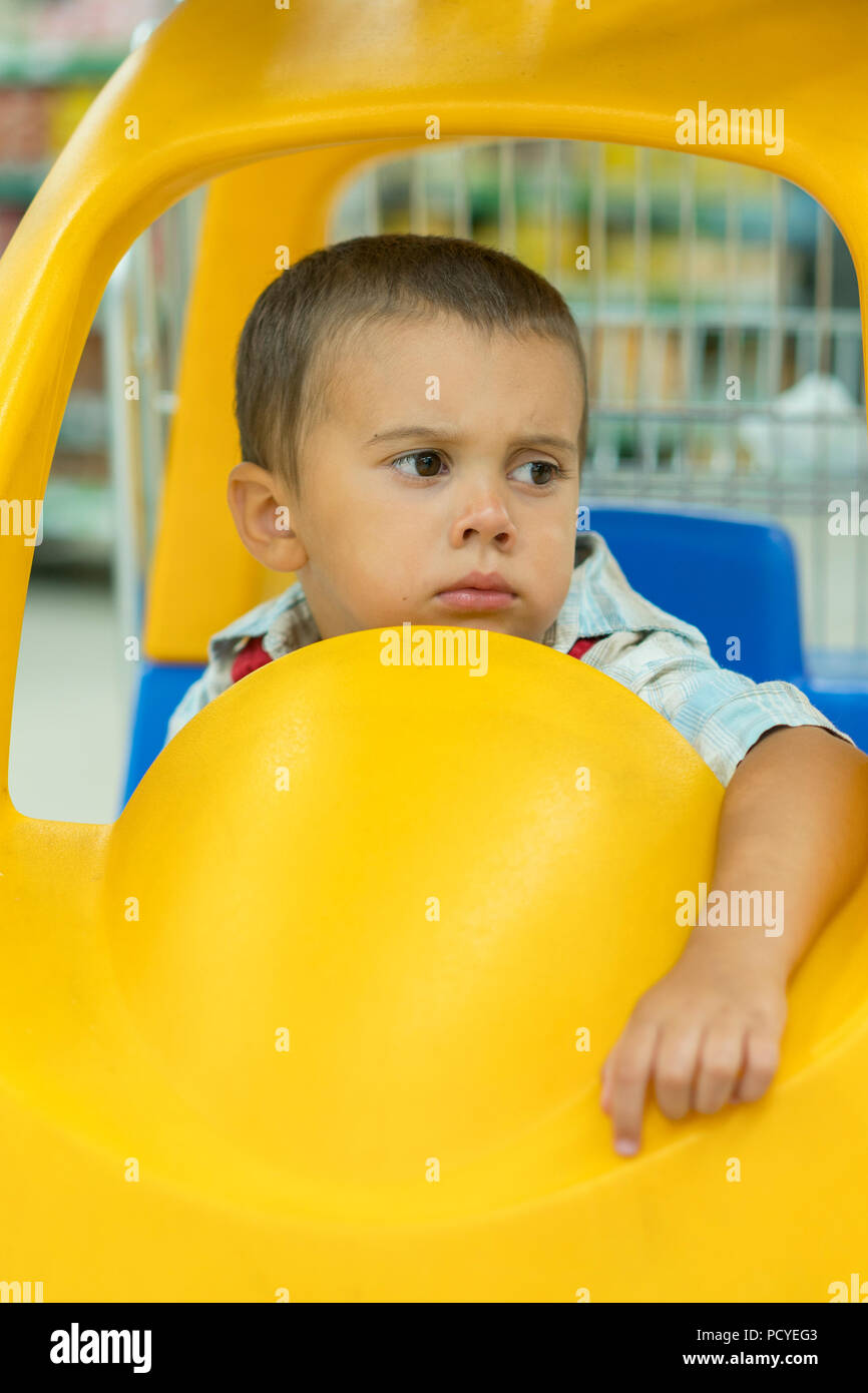Cute sad little 2 year old baby boy child in the little toycar trolley