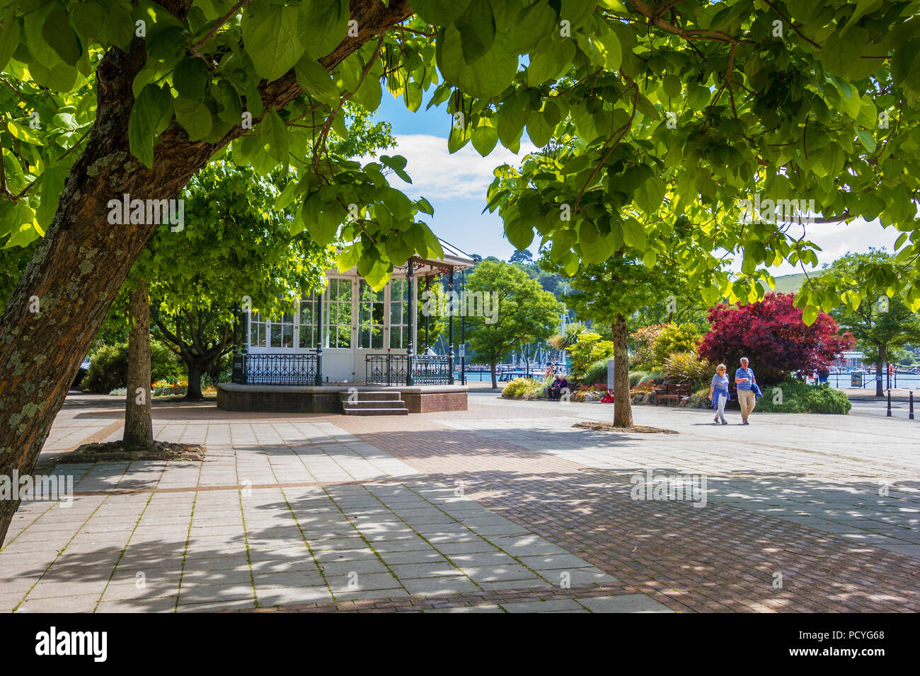 A view of the bandstand in The Royal Avenue Gardens, framed by a branch and trunk of an Indian Bean Tree in Dartmouth in South Devon, UK. Stock Photo