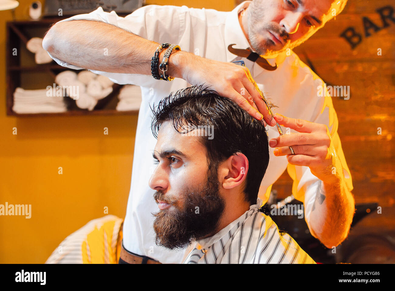 Barber shears hair on her head with a young handsome guy with a beard and mustache. Barber Shop
