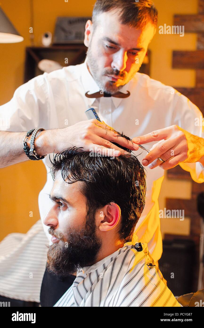 Barber shears hair on her head with a young handsome guy with a beard