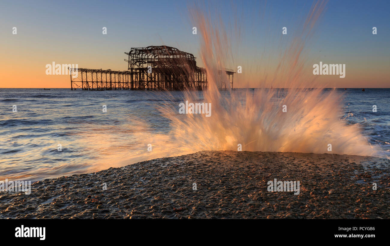The ruins of the West Pier in Brighton at sunrise with sea water plashing up against a groyne due to the incoming tide Stock Photo