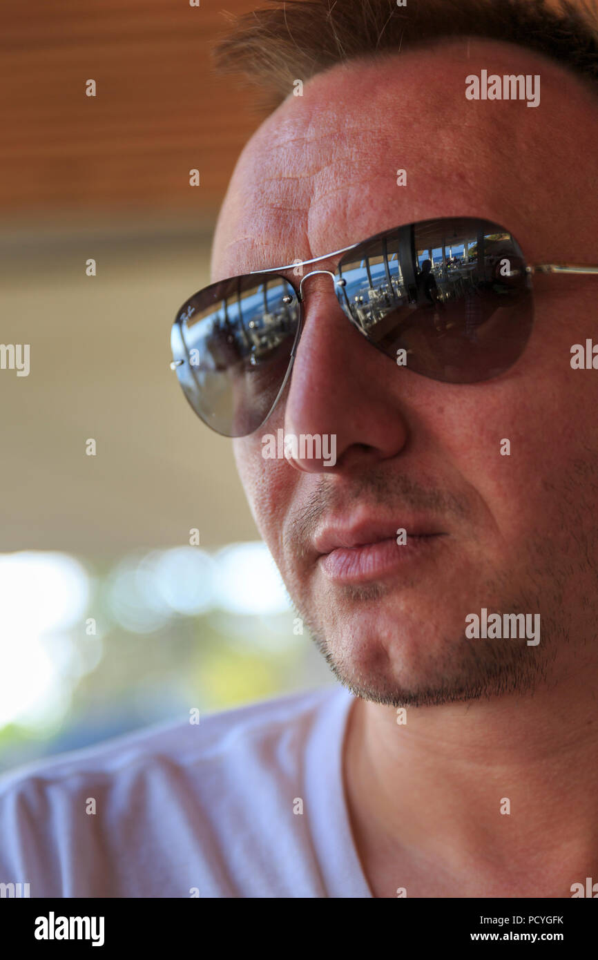 A young man stands in a chiringuito (beach bar) on the Costa del Sol, Spain, the view of the Mediterranean is reflected in his sunglasses Stock Photo
