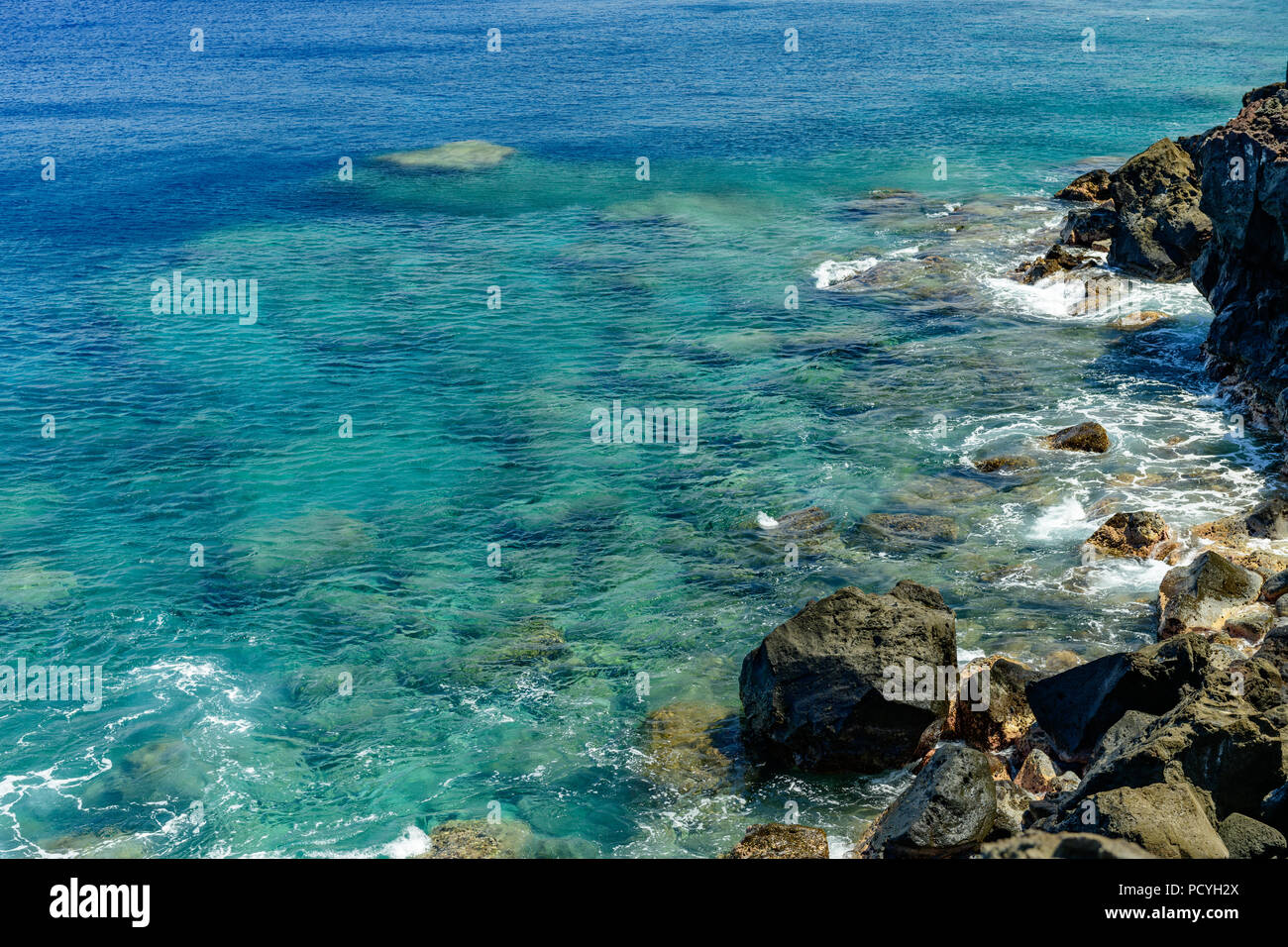 Ka Lae or South Point on the Big Island of Hawaii looking downward at clear water off a rocky cliff. An inviting location for snorkel or scuba. Stock Photo
