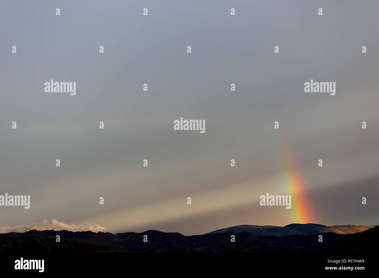 Beautiful and surreal view of part of a rainbow over some hills Stock Photo