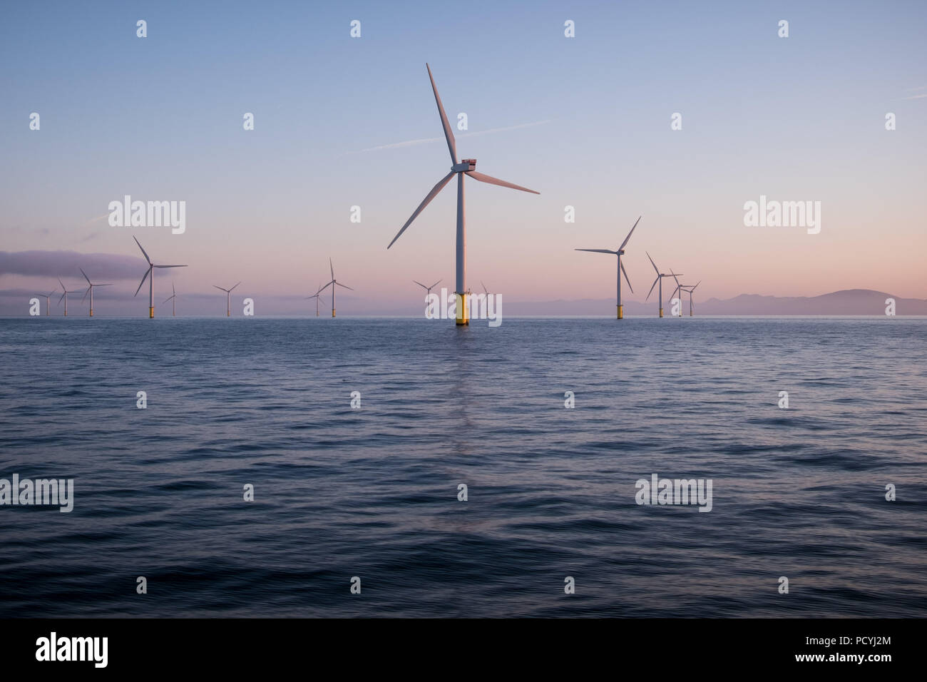 Offshore wind turbines at dawn in the Irish Sea, UK, with the Lake District National Park seen in the distance Stock Photo