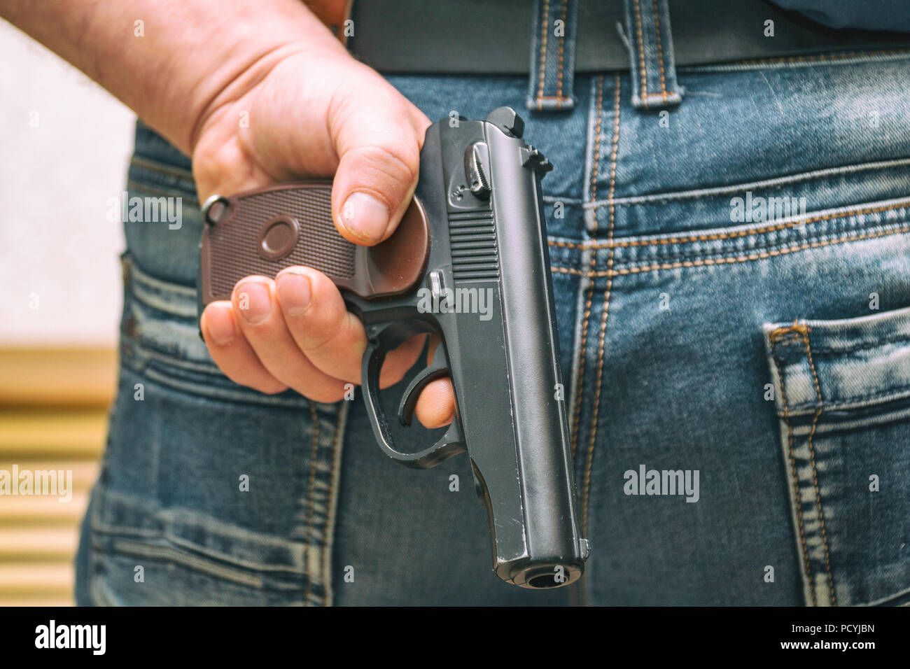 Man in jeans holding a gun behind his back Stock Photo