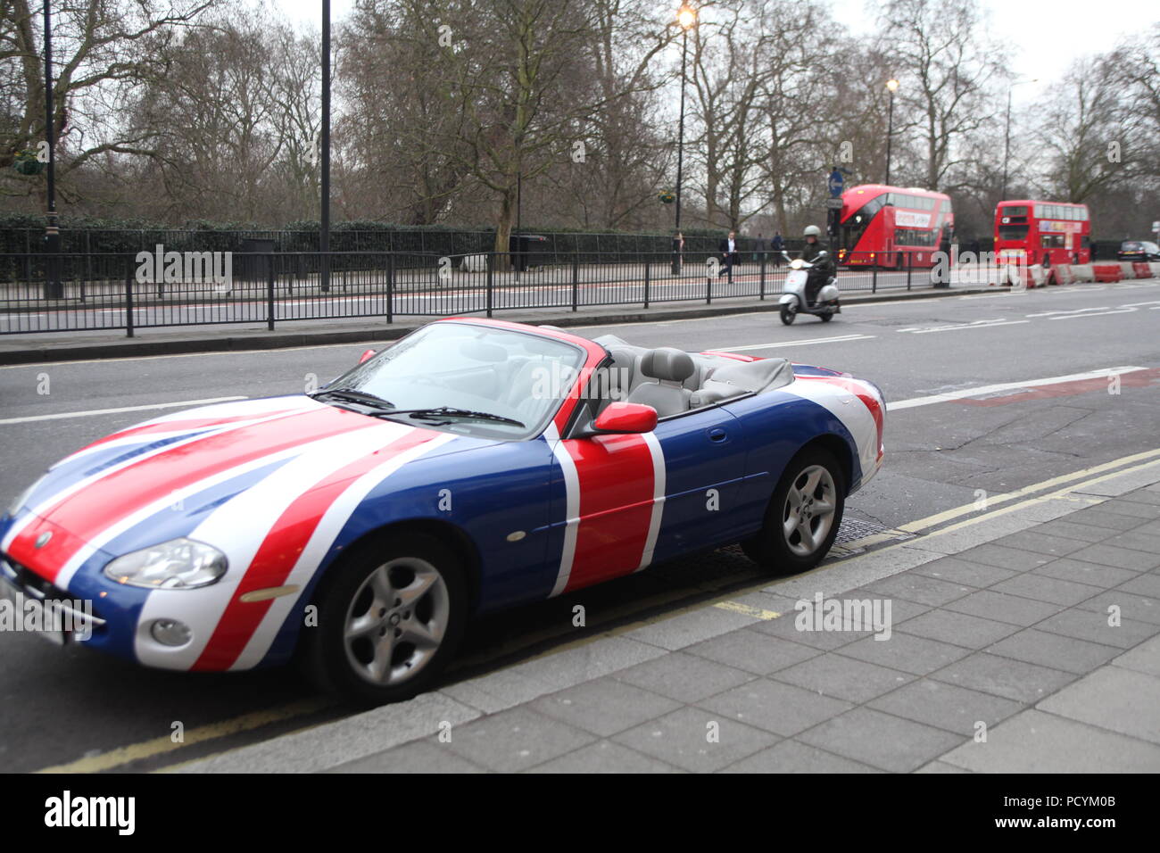 Cabriolet type sport Union Jack painted car parked at Park Lane near Grosvenor House Hotel on chilly winter day, with two double-deckers in background Stock Photo