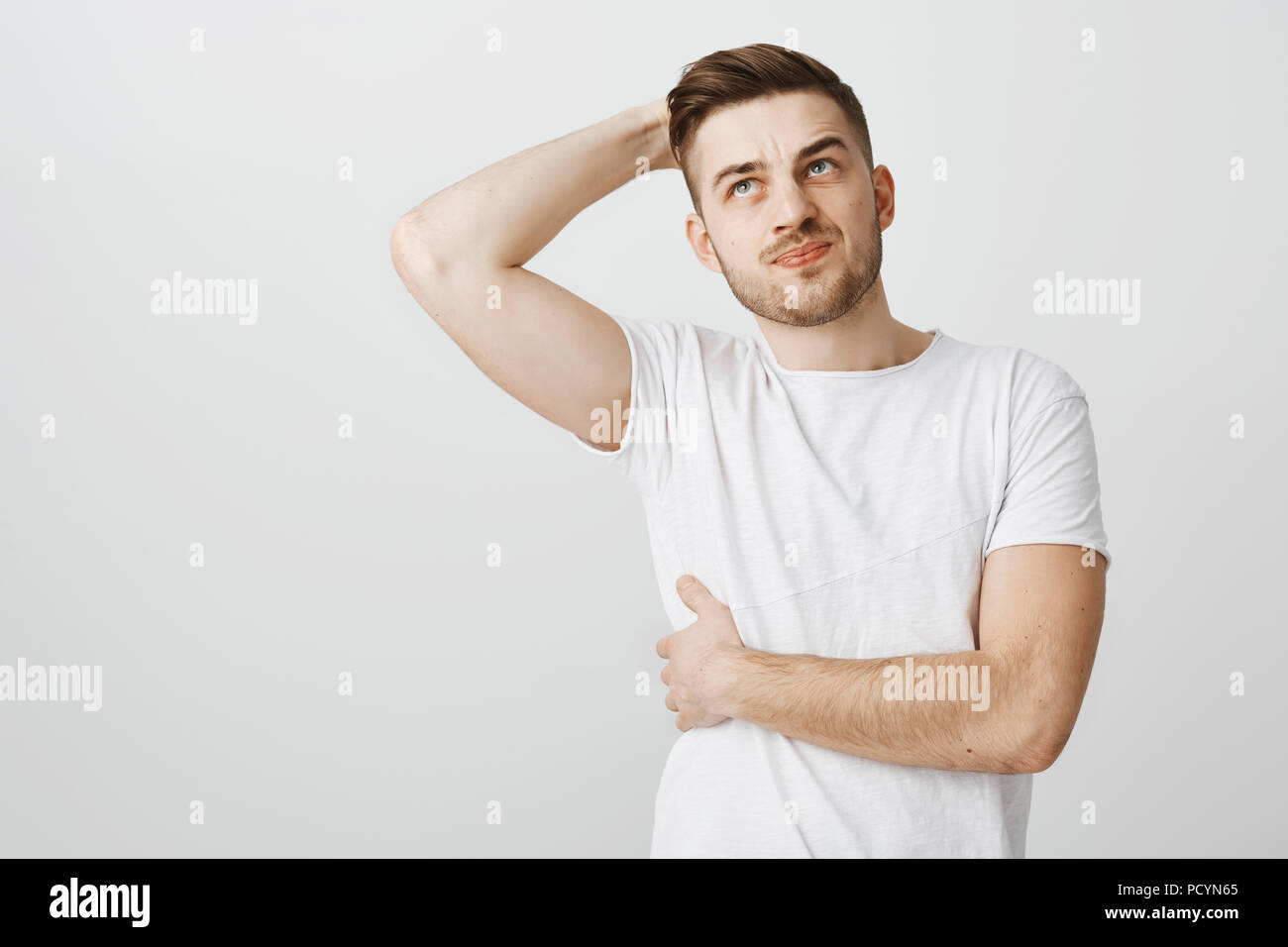 Attractive unshaven sportsman feeling pain in chest touching bone, smirking from painful feeling spraining mascule during workout in gym raising and h Stock Photo