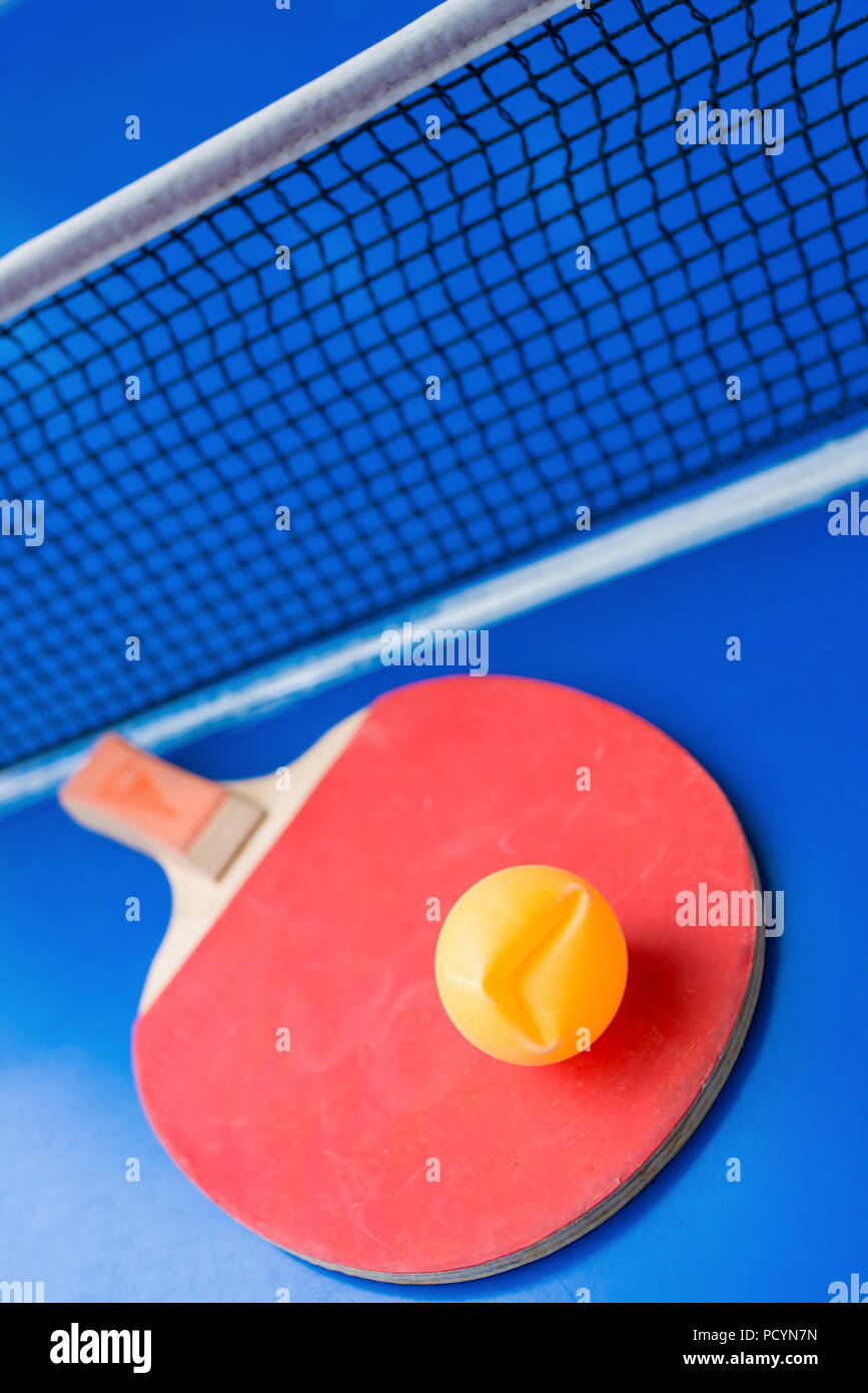 old pingpong racket and a dented ball on a blue pingpong table Stock Photo