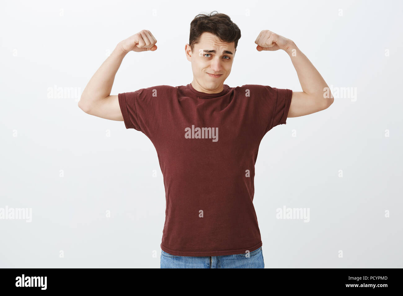 Look how strong I am. Portrait of self-assured handsome european guy in red t-shirt, raising arms and showing muscles with confident expression, bragg Stock Photo