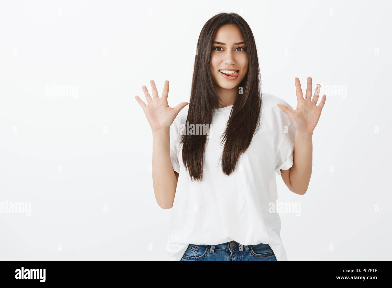 Jazz hands makes day brighter. Childish playful funny girl with long dark hair in casual outfit, raising palms and sticking out tongue, making faces w Stock Photo