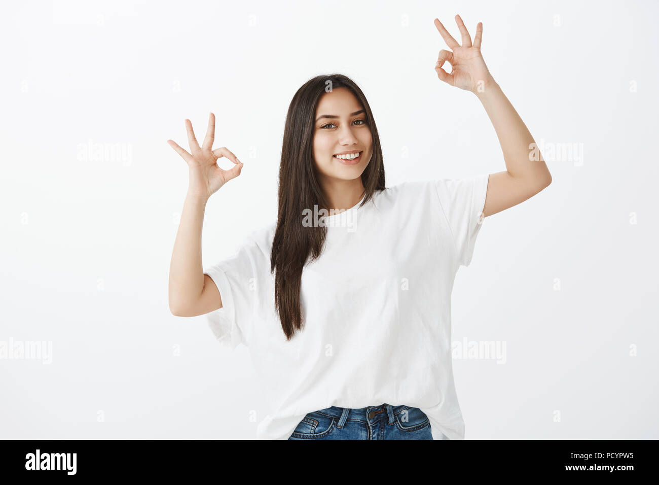 Say okay. Portrait of friendly-looking happy woman in white t-shirt and jeans, raising hands with great or acception gesture, giving approval and smil Stock Photo