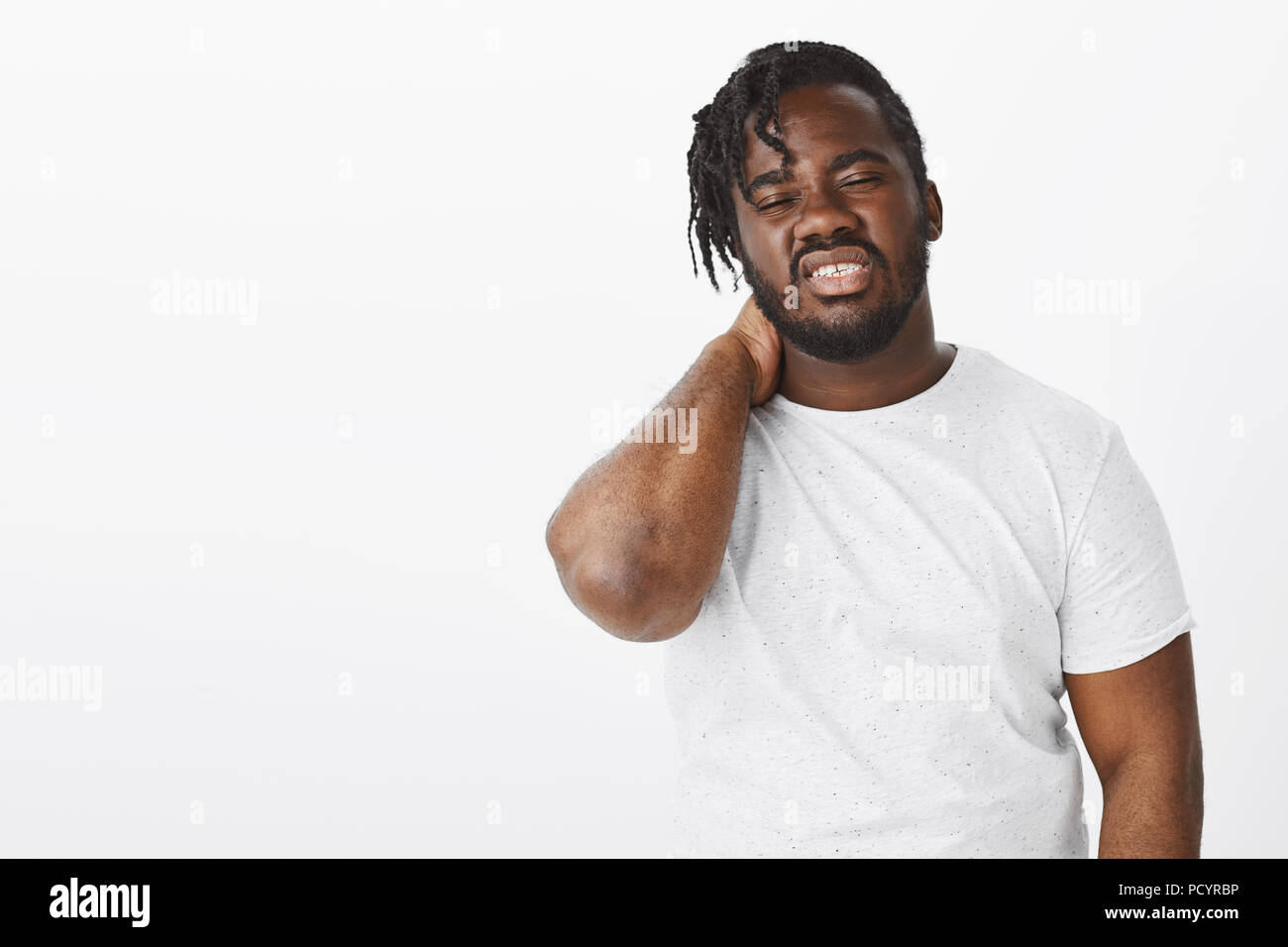 Tired displeased attractive darkskinned guy in white tshirt, rubbing