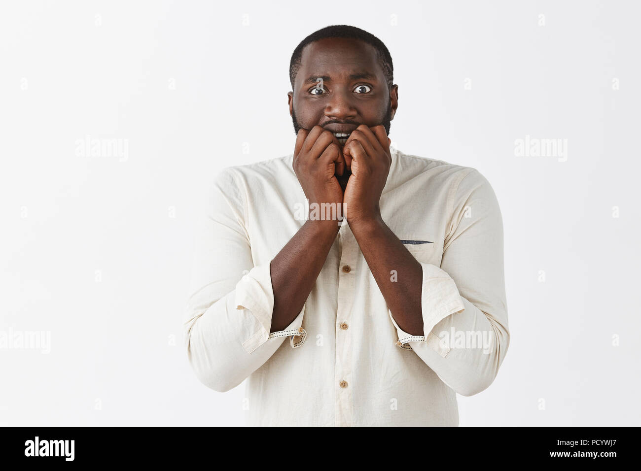 Man gets frightened hearing scary stories of friend. Scared intense and  nervous attractive African American with short haircut in white shirt,  biting Stock Photo - Alamy