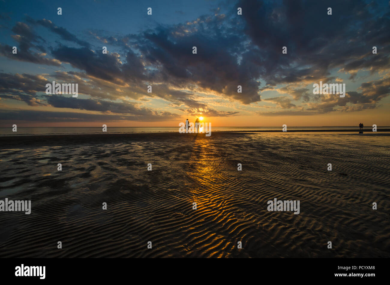 Two people walking along the beach in the sunset Stock Photo - Alamy