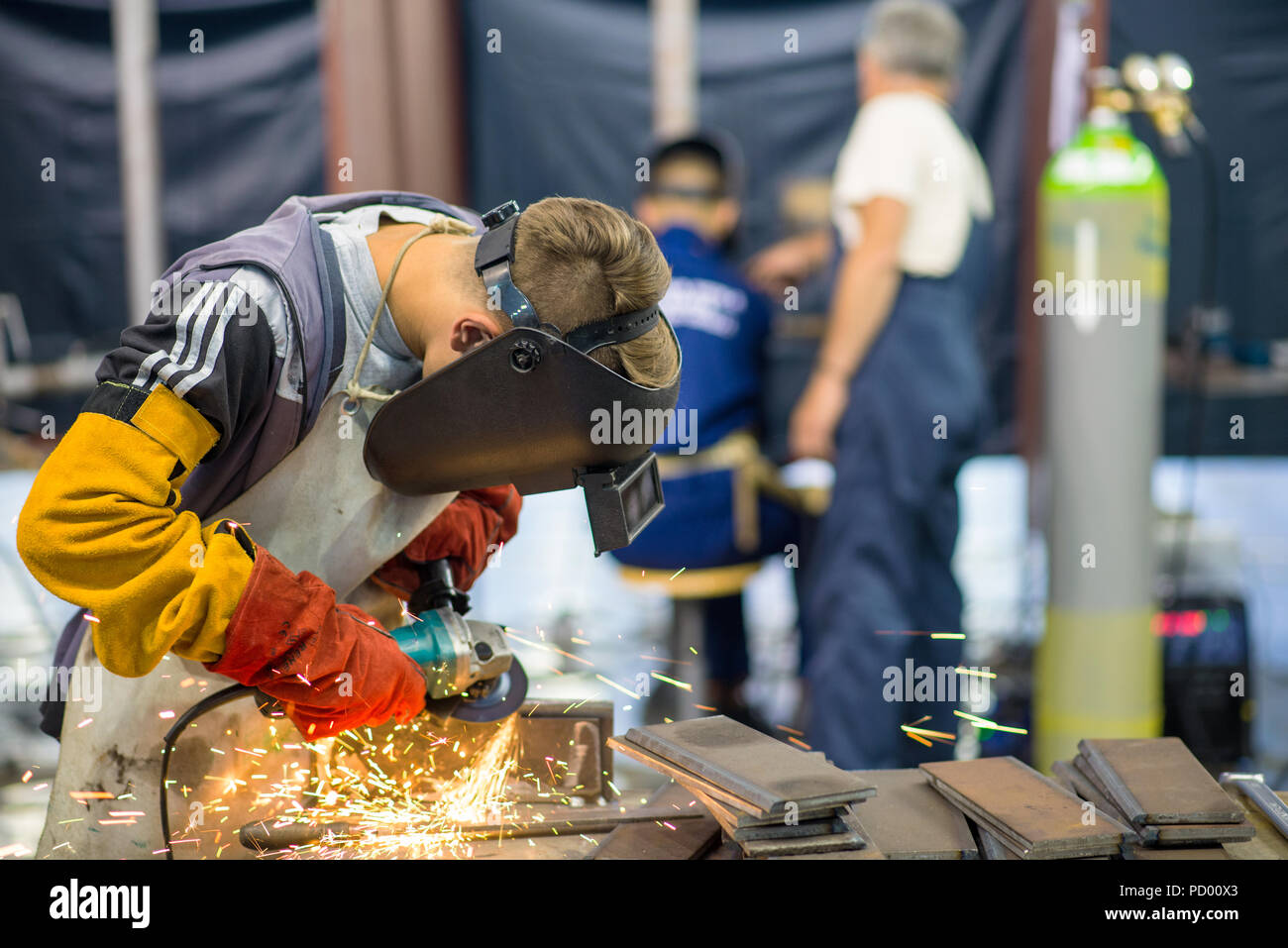 Belgrade, Serbia - May 23, 2018: Welder working in a factory with two blurry workers in the background Stock Photo