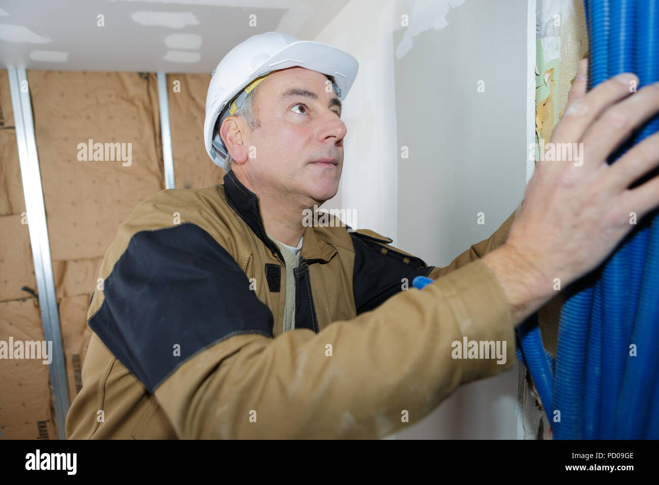 Tradesman fitting conduit into wall cavity Stock Photo Alamy