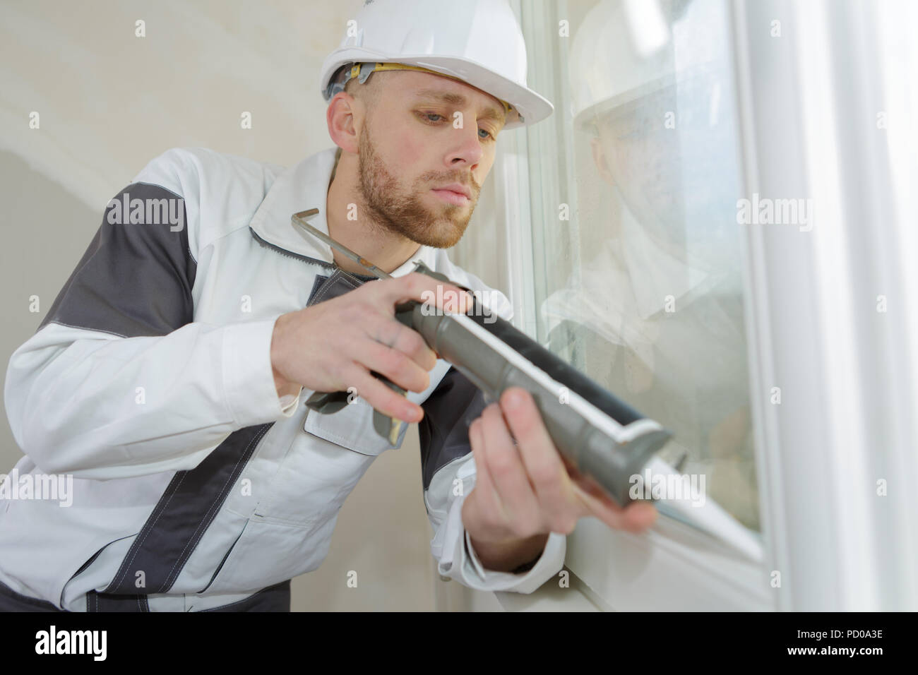 young construction worker sealing window in house Stock Photo