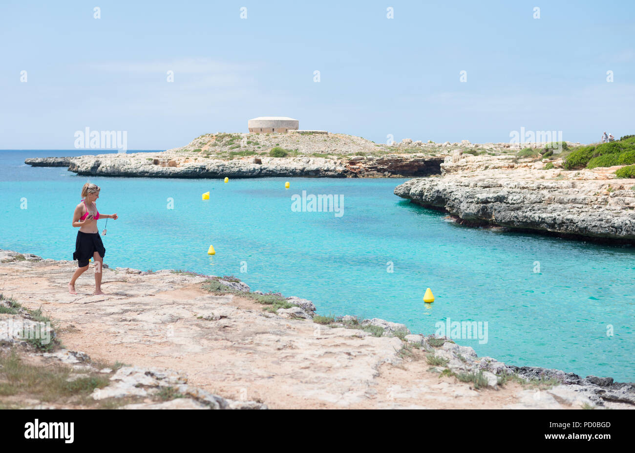 A woman walks along the coast near Torres Des Castellar in Menorca, Spain Stock Photo