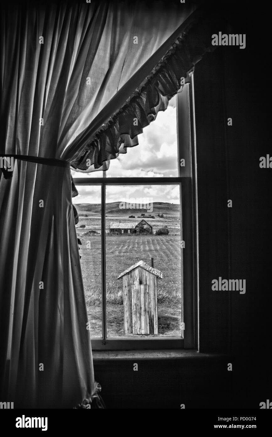 A unique view of a rural outhouse, through the old farmhouse window of the main house to which it belonged. Original photo has been desaturated to inc Stock Photo