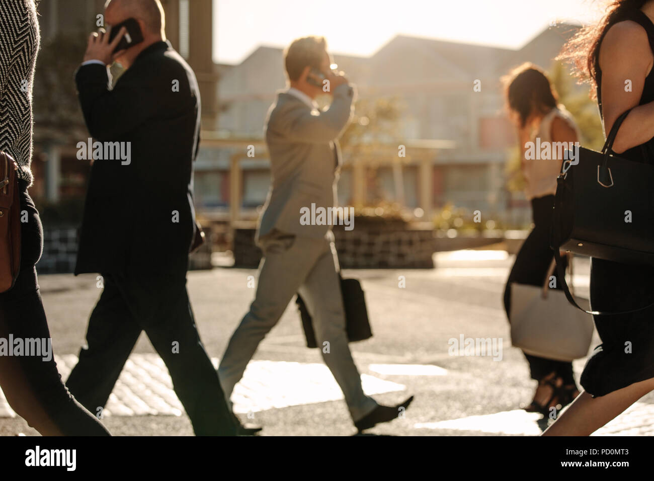 Men and women using mobile phone while commuting to office on a crowded street with sun flare in the background. People leading a busy life using mobi Stock Photo