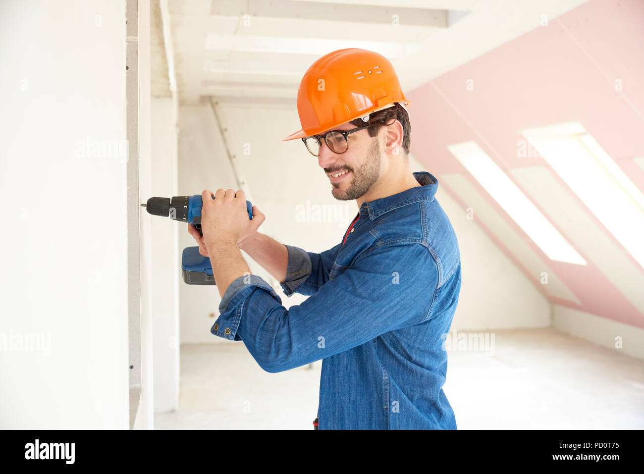 Successful young handyman using hammer drill driver at construction site. Stock Photo
