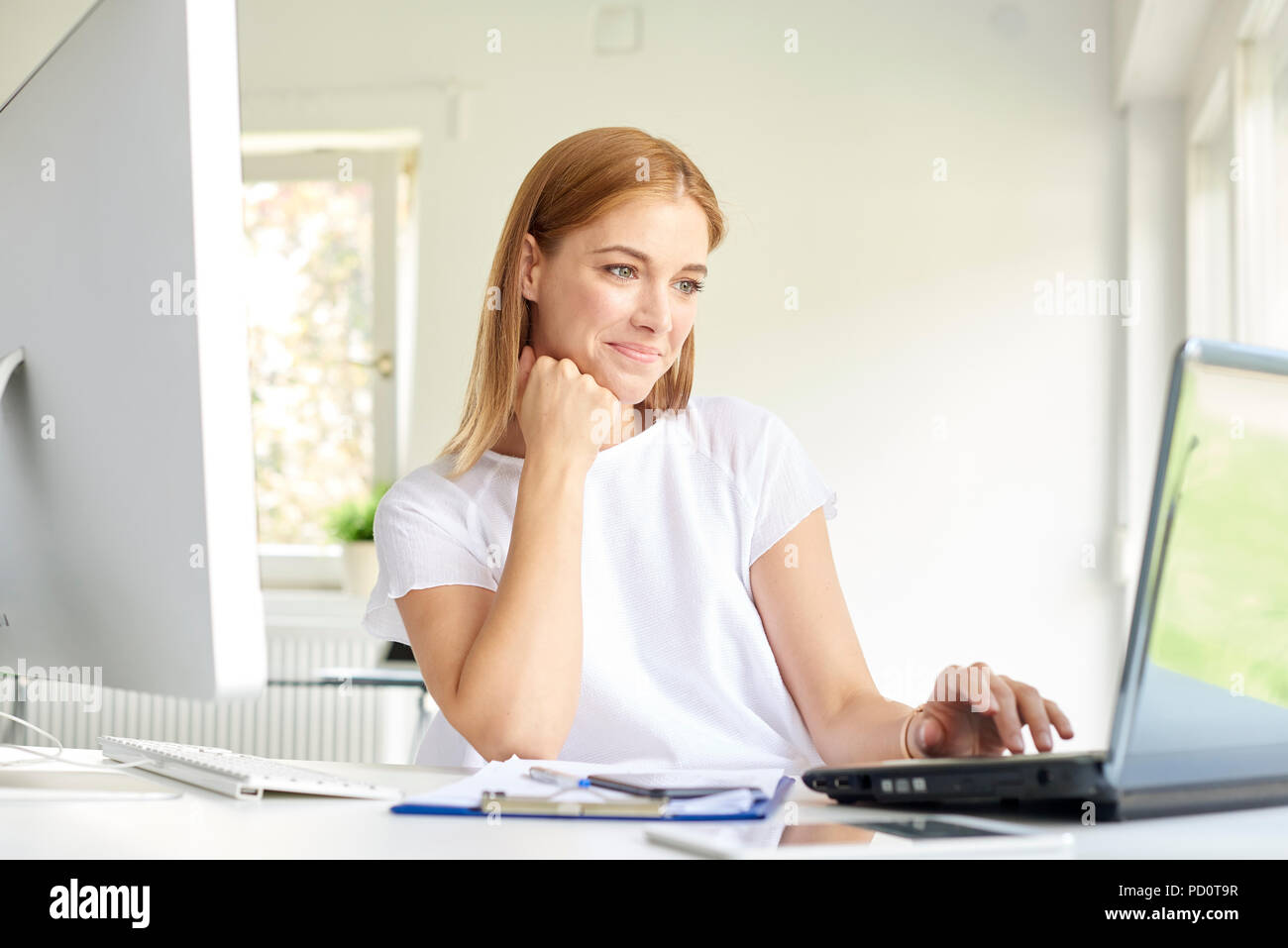 Shot of smiling young businesswoman looking thoughtully while using her laptop at the office. Stock Photo