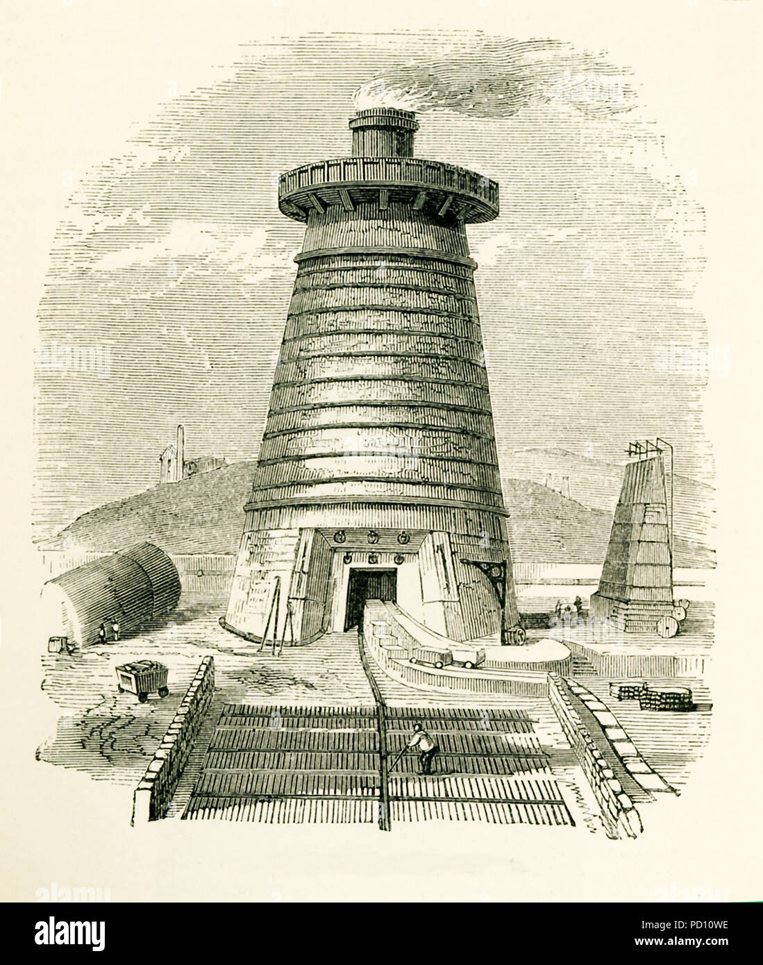 This illustration dates to the 1870s and shows a blast furnace in Great Britain, where the enormous quantity of iron produced from clay ironstone was first obtained in the state of cast iron by the process of smelting. In thisprocess the clay ironstone is roasted after having been broken up into lumps. When ready, the ore is then put in a blast furnace (seen here), a structure about 40 to 50 feet high and 12 to 17 fet in internal diameter at its widest part. Stock Photo