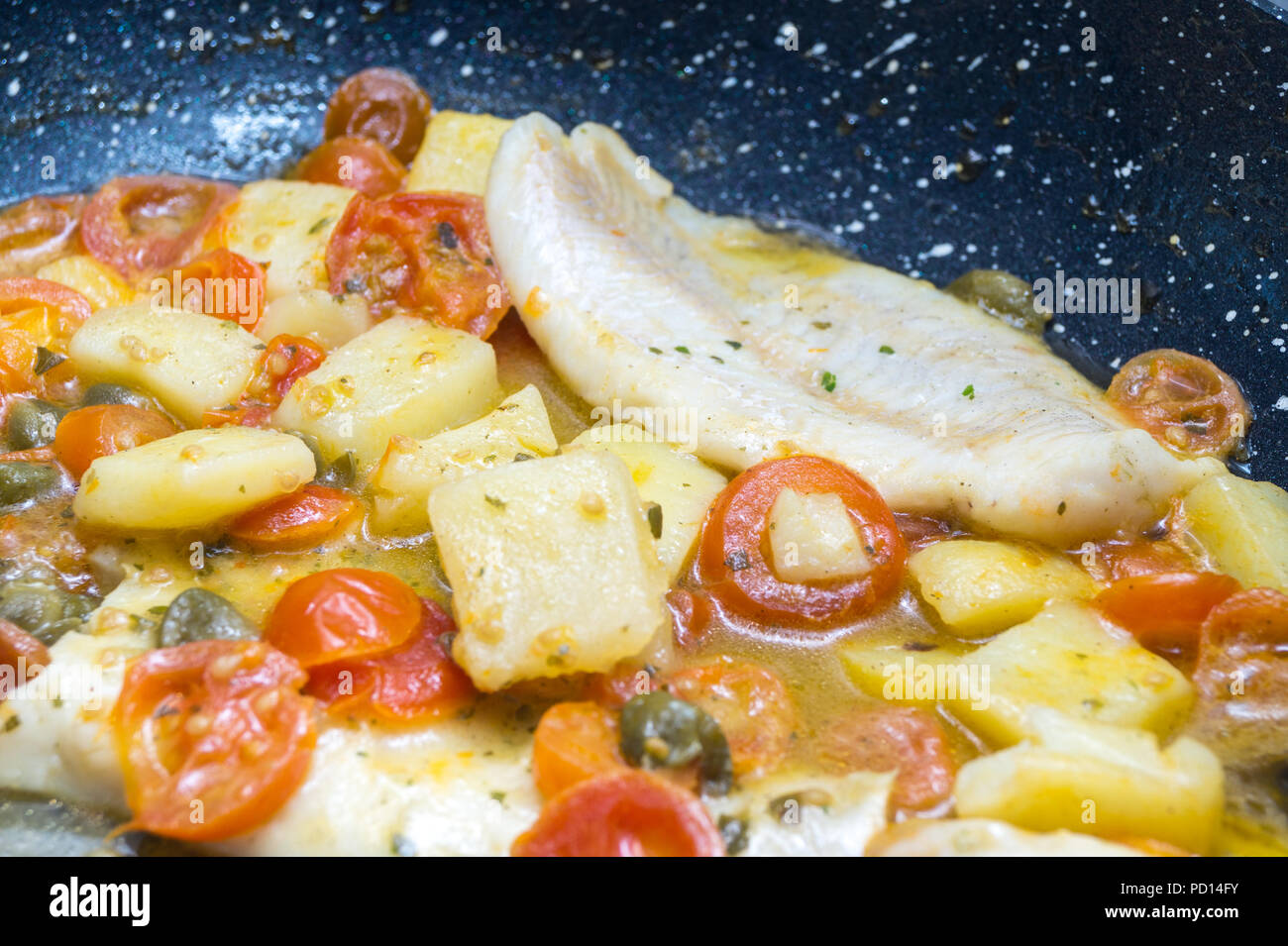 cod cooked in a pan, with tomato, potatoes and capers Stock Photo