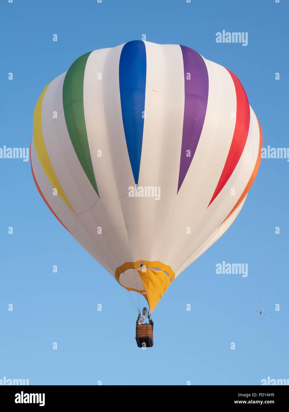 A colorful striped hot air balloon in flight against cloudless blue sky ...