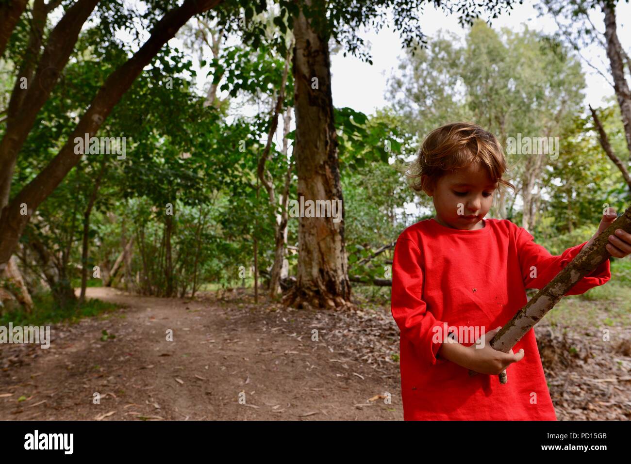 Child looks at a stick she has just picked up, Booroona walking trail on the Ross River, Rasmussen QLD 4815, Australia Stock Photo