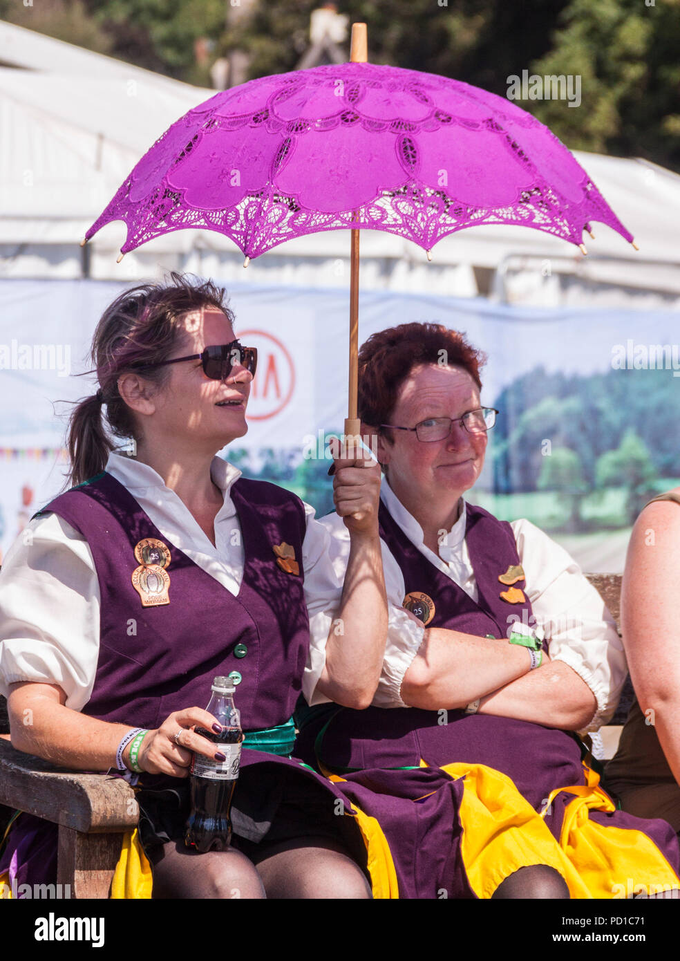 Sidmouth, UK 5th Aug 18 Clog dancers waiting their turn at Sidmouth Folk Festival cool off under a parasol as temperatures again soar on the Devon coast. Photo Central / Alamy Live News Stock Photo