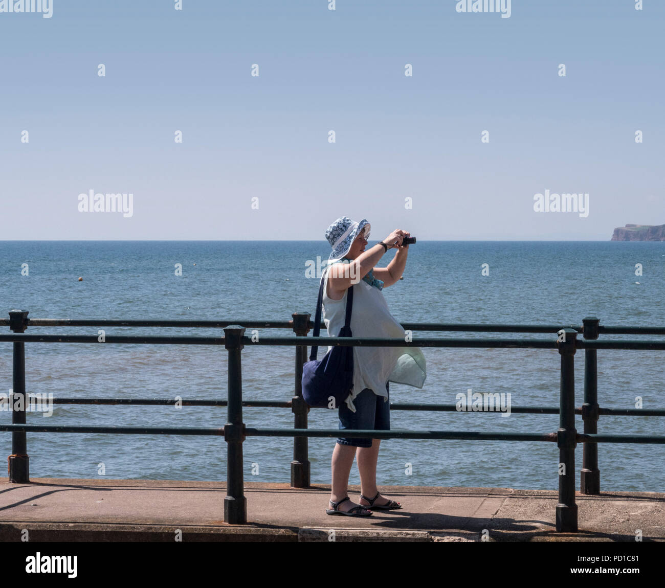 Sidmouth, UK 5th Aug 18 A lady takes pictures on the seafront at Sidmouth as temperatures again soar on the Devon coast. Photo Central / Alamy Live News Stock Photo