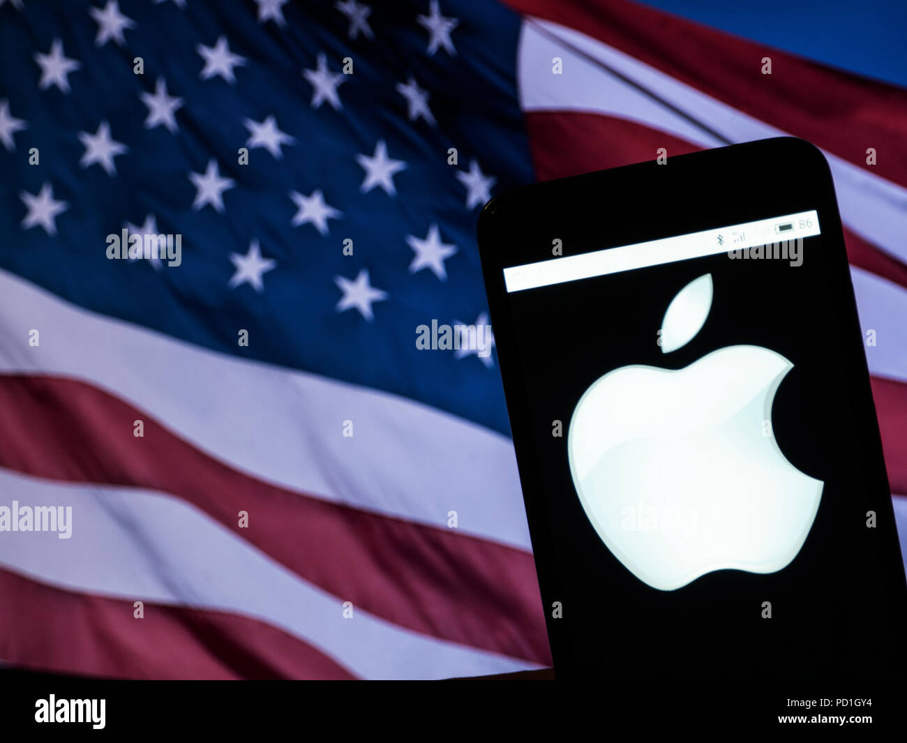 KIEV, UKRAINE - Aug. 4, 2018: The Apple logo seen displayed on a smart phone with a background of an American Flag. Apple's capitalization exceeded $1 trillion Stock Photo