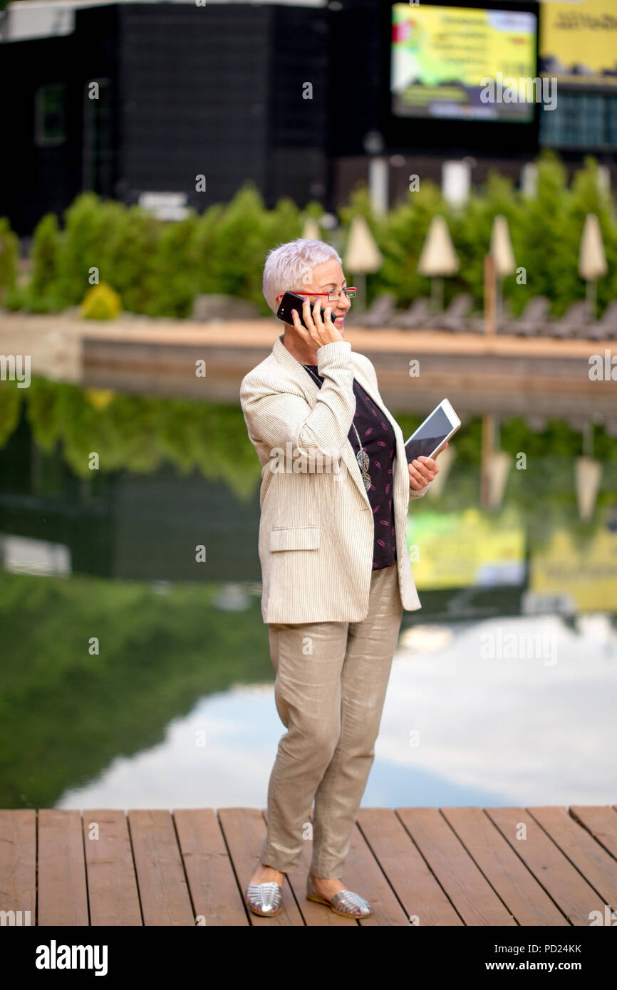 full length portrait of positive mature woman making a phone call in the resort Stock Photo