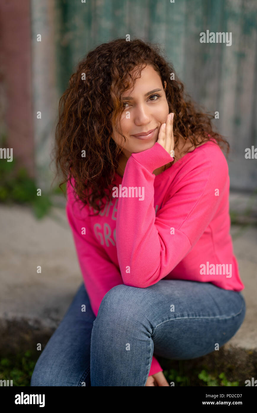 Close up portrait of a cheerful curly young woman smiling outdoors. Stock Photo