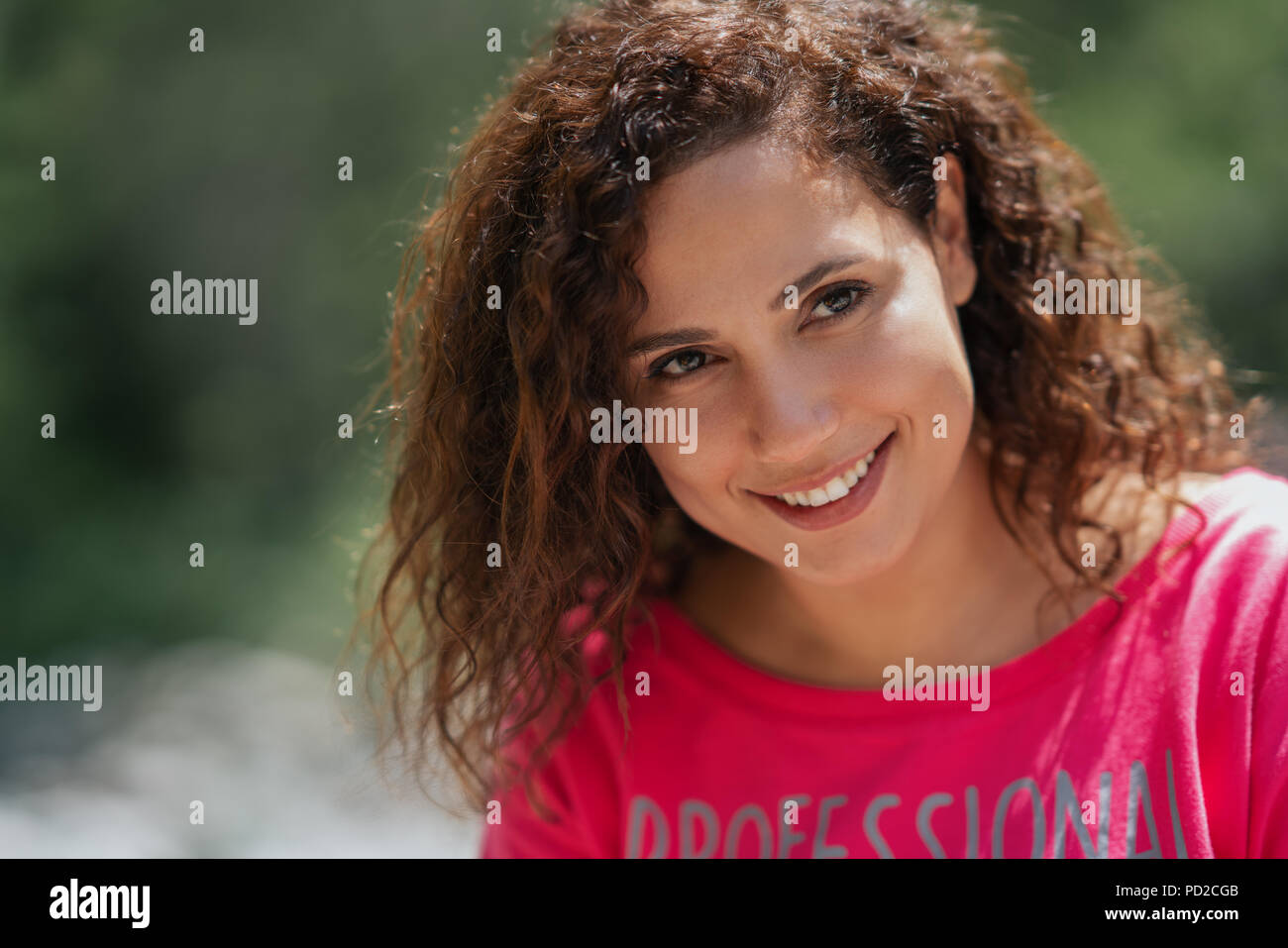 Close up portrait of a cheerful curly young woman smiling outdoors. Stock Photo