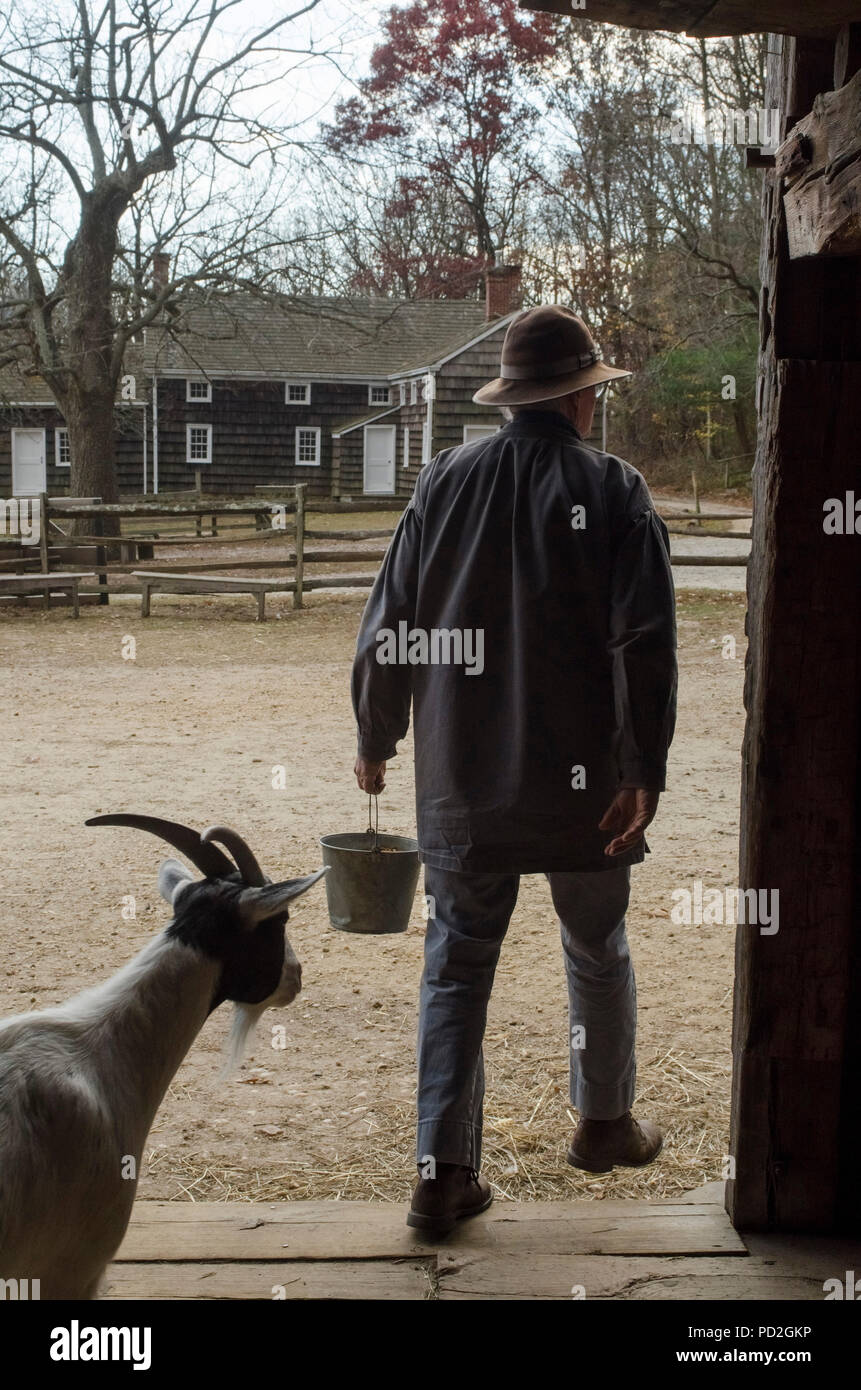 Farm worker and goat walk out of a barn at the Old Bethpage Village