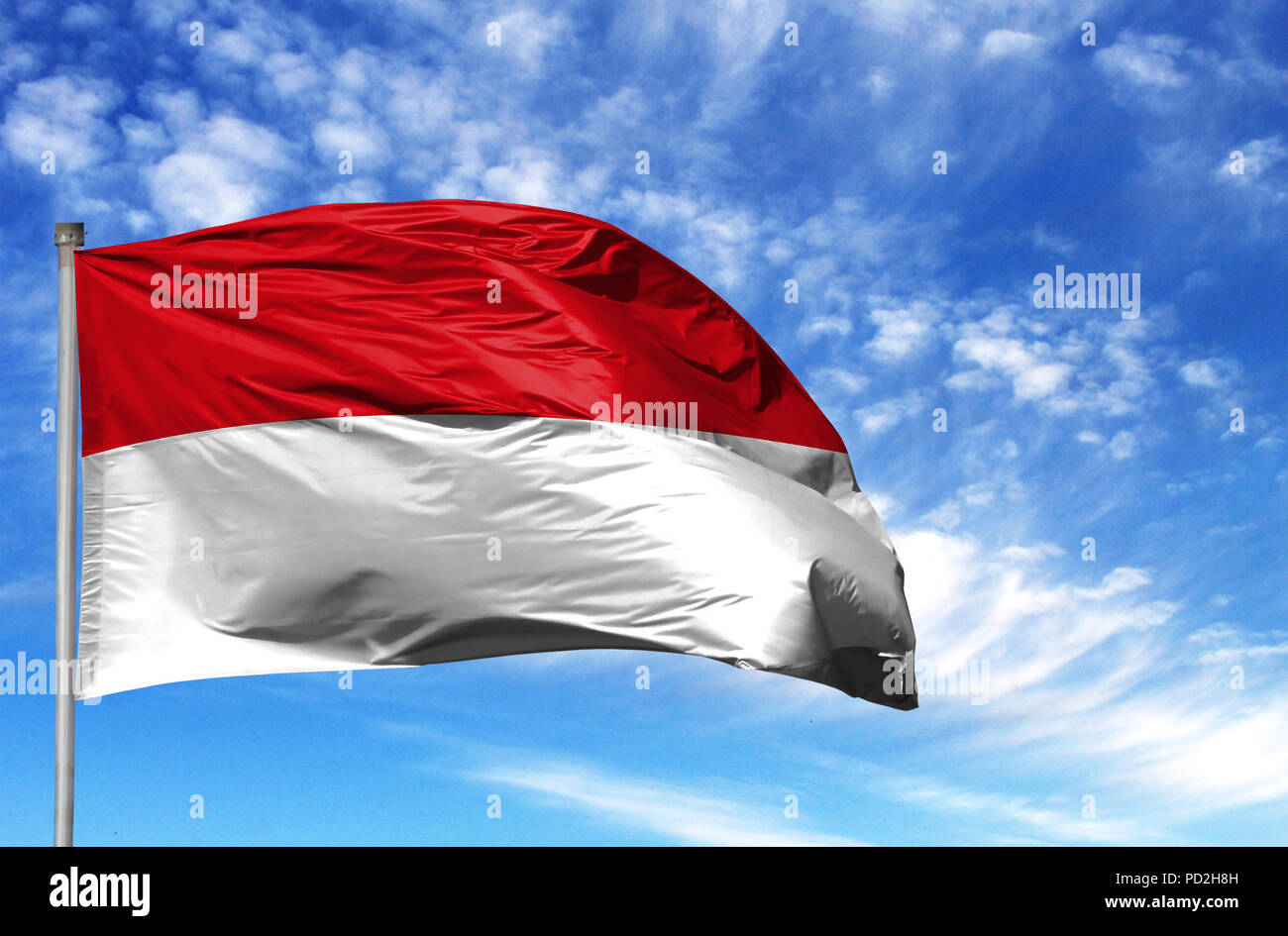 National flag of Monaco on a flagpole in front of blue sky. Stock Photo
