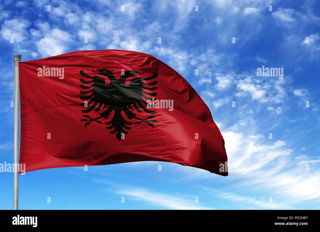 National flag of Albania on a flagpole in front of blue sky. Stock Photo