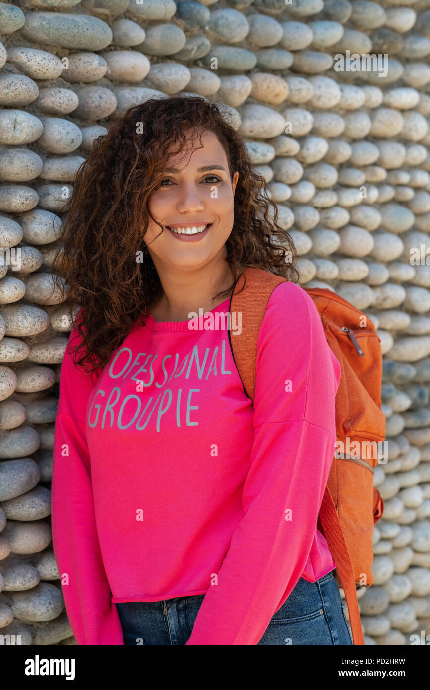 Close up portrait of a cheerful curly young university student woman smiling outdoors. Stock Photo
