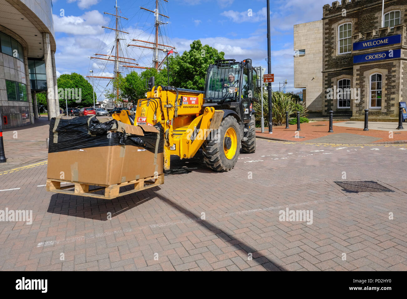 Cardiff Bay, Cardiff, Wales - May 20, 2017: Yellow JCB vehicle with a driver, moving a large cardboad covered box in a street near Cardiff Bay. Stock Photo