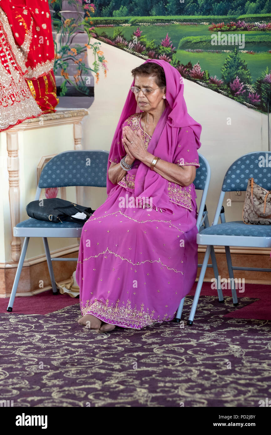 An older female worshipper in a beautiful sari prays & meditates at a Hindu temple in Richmond Hill, Queens, New York. Stock Photo