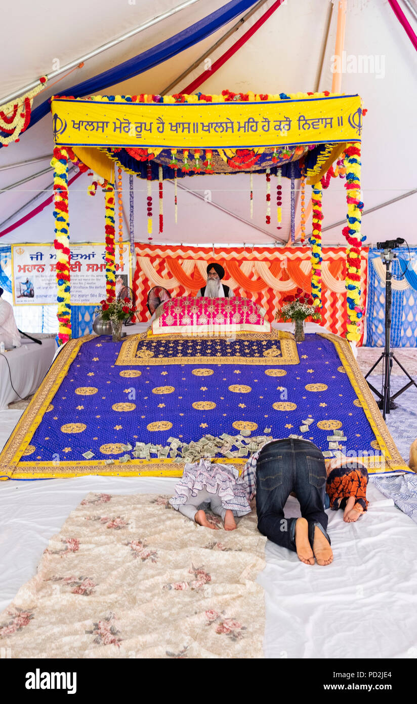 A father and 2 children bowing in prayer at an outdoor Sikh prayer session in a tent in Smokey Park, Richmond Hill, Queens, New York Stock Photo