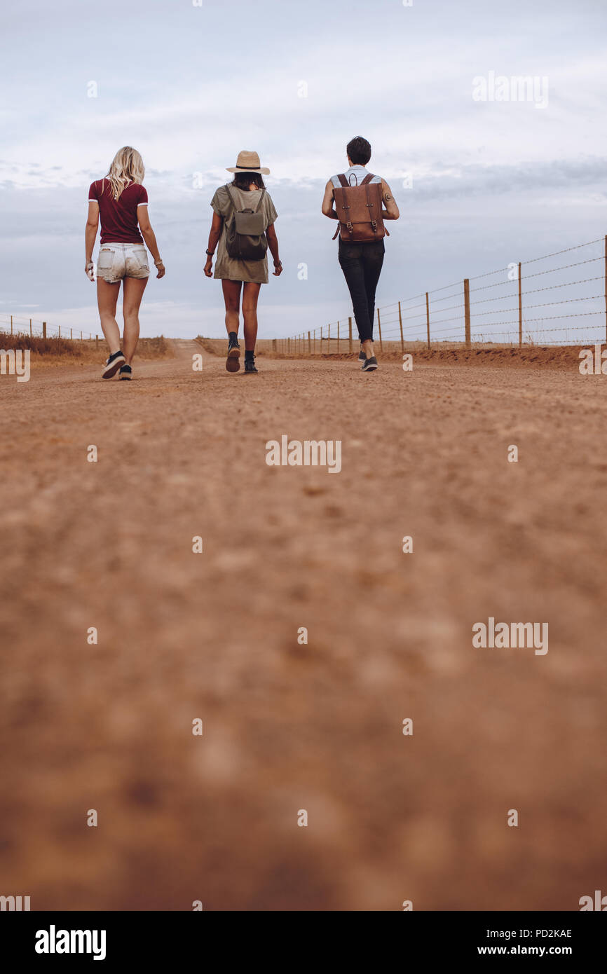 Vertical shot of three women friends together walking down the country road leaving their car behind. Female friends walking on a rural road after the Stock Photo