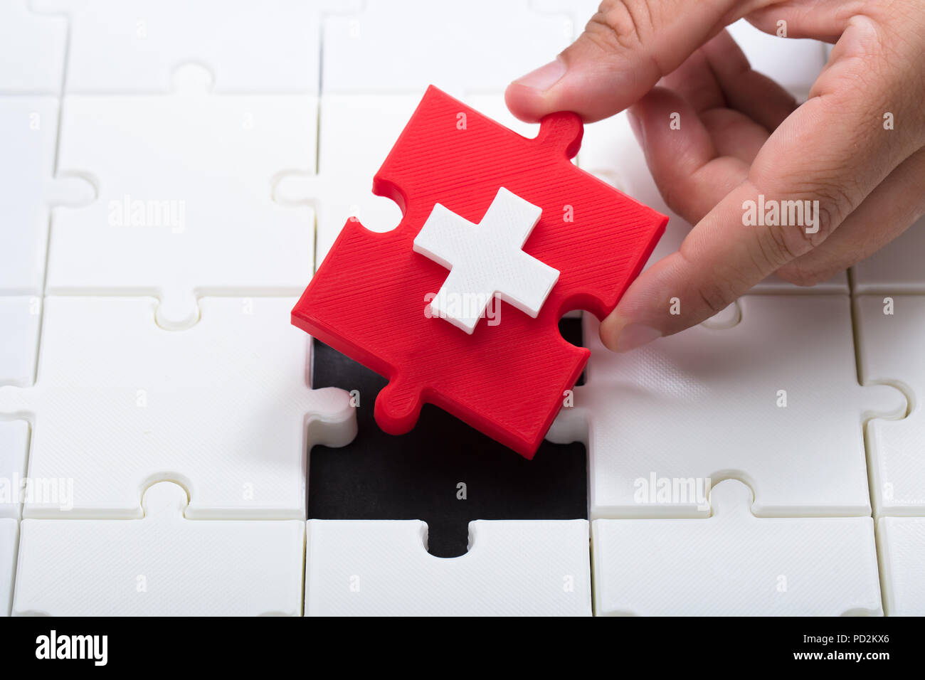 Man's hand solving jigsaw puzzle with red piece having first aid