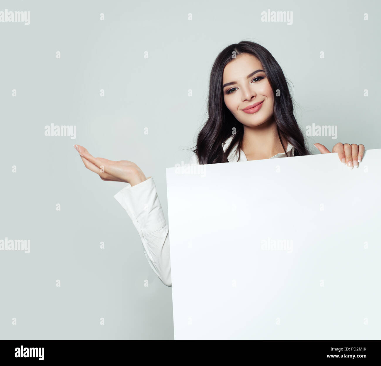 Happy business woman showing empty open hand and holding white blank paper banner background. Young woman smiling, business and education concept Stock Photo