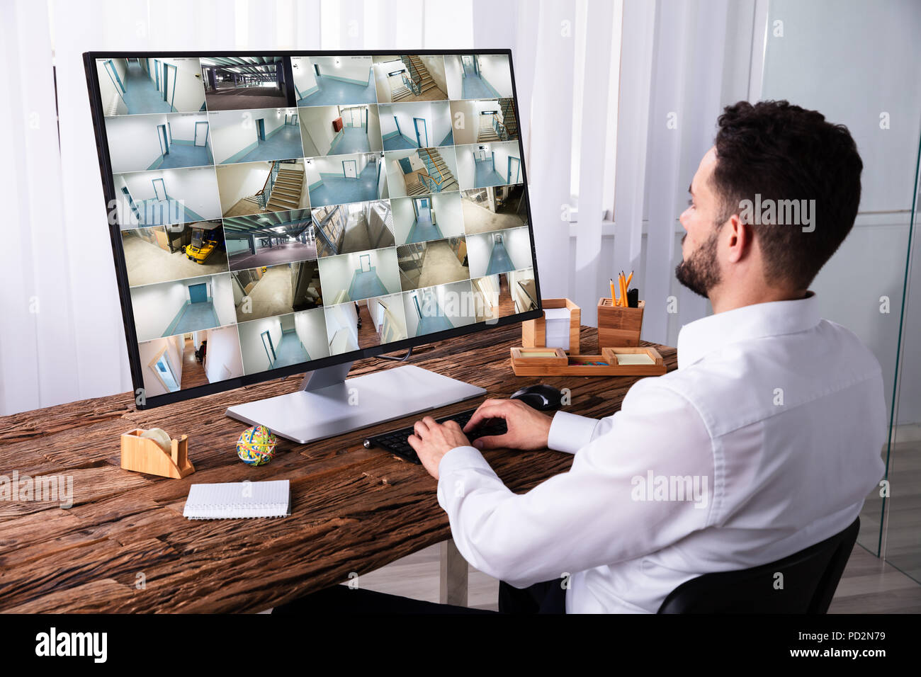 Young Businessman Monitoring CCTV Camera Footage On Computer Over Wooden Desk Stock Photo