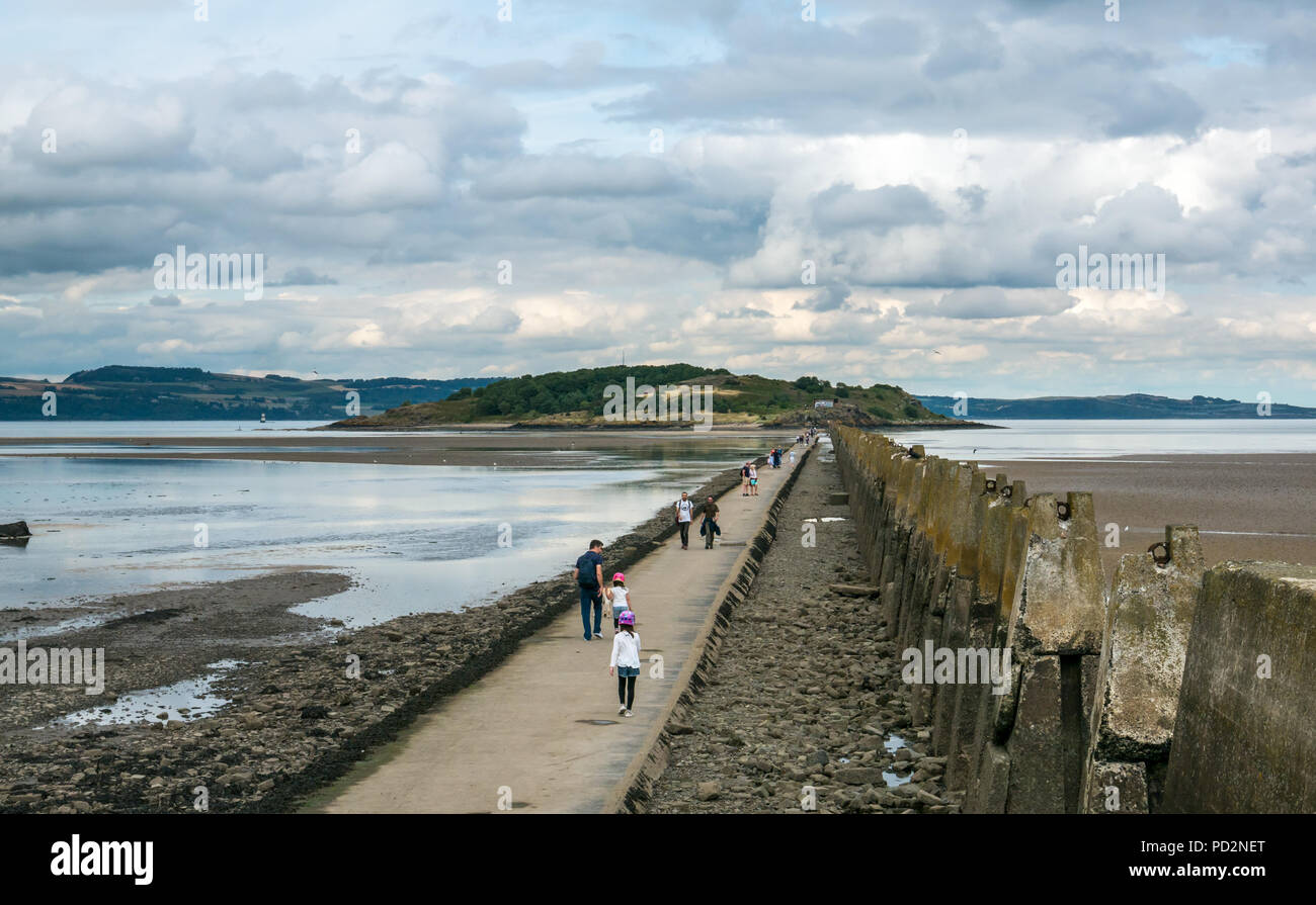 People walking on tidal causeway to Cramond Island with World War II anti ship barrier with remains of worn concrete pylons, Edinburgh, Scotland, UK Stock Photo