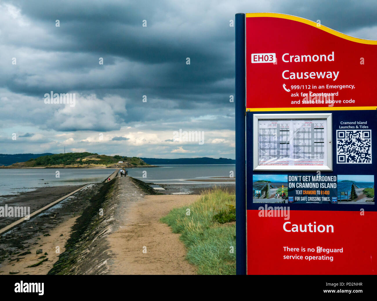 Tidal causeway with World War II concrete ship barrier to Cramond Island with notice about safety and tide times, Cramond, Edinburgh, Scotland, UK Stock Photo